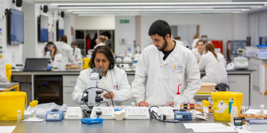 Two students working in a science laboratory with equipment on the table in front of them