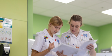 Two student nurses looking down at clipboards in the mock hospital ward
