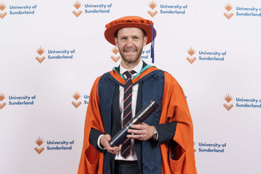 Man standing in graduation robes holding a scroll
