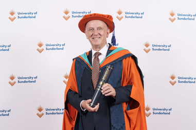 Man standing wearing graduation ceremony robes and holding a scroll