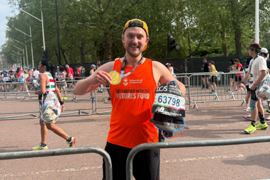 Alumnus holding medal on the street at the London Marathon