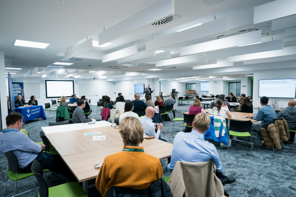 Crowd of attendees sat at tables while academic presents