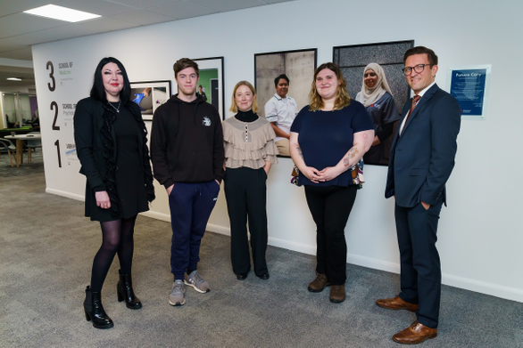 Academics and students stood in front of photographs on the wall