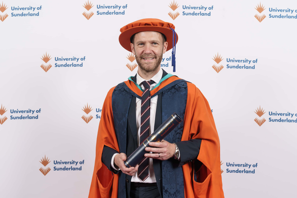 Man standing in graduation robes holding a scroll