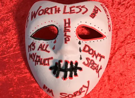 A white mask with worthless written on it in pen on a red background