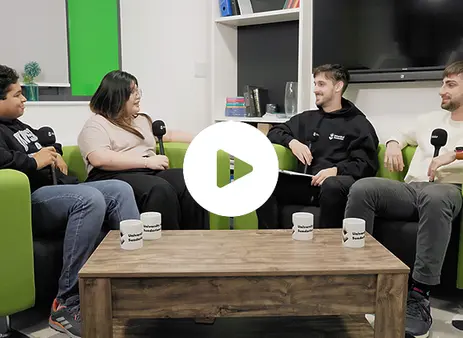 Four students sitting on the sofa one with a microphone all chatting with a play button overlay