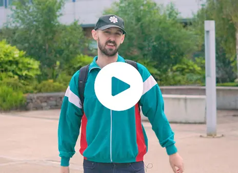A student standing facing the camera with a play button overlay