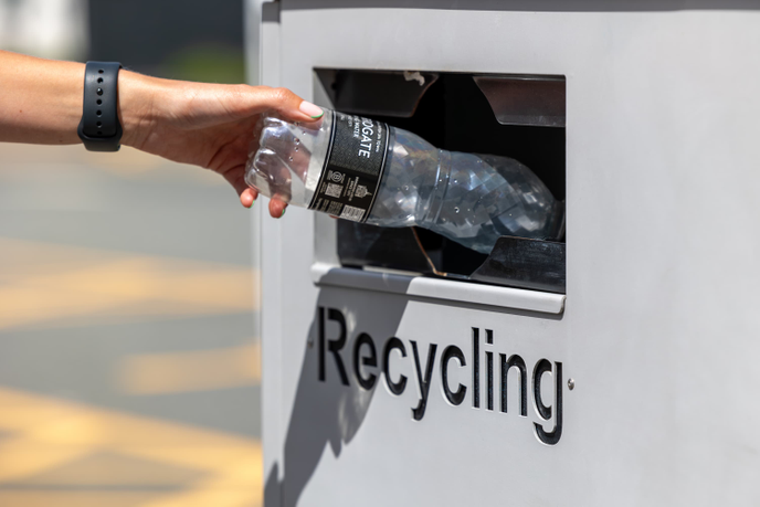 A hand leaning into a recycling bin with a plastic bottle