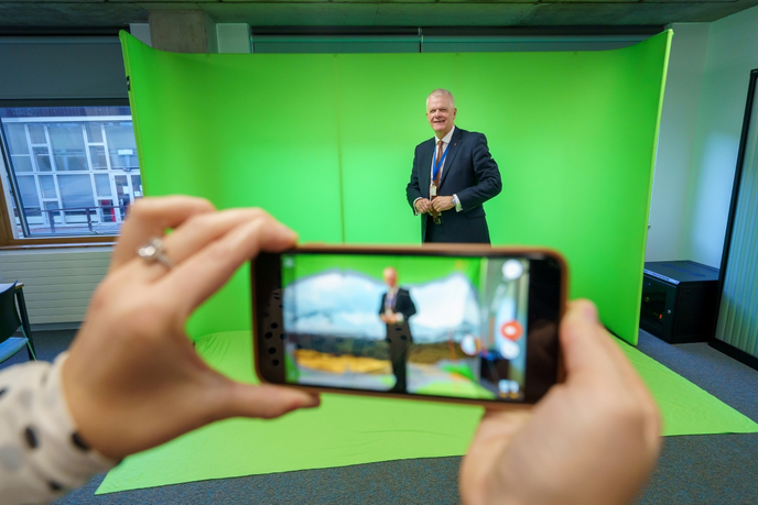 Vice-Chancellor stood behind phone camera next to greenscreen