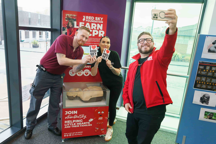 Three people standing next CPR simulator