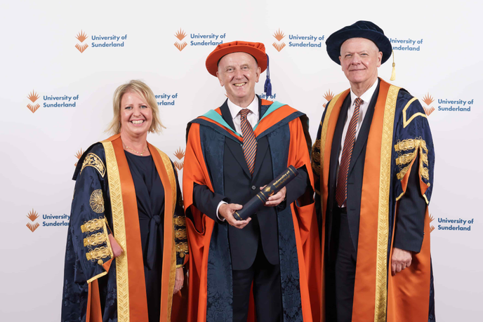 Three people standing in graduation ceremony gowns