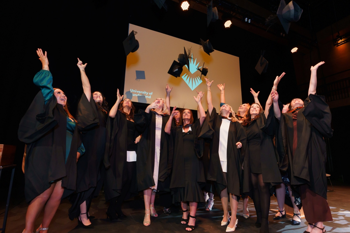 Graduates in gowns throwing their caps on a stage