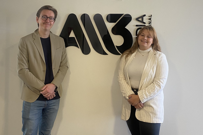 Two students standing next to a logo on a wall