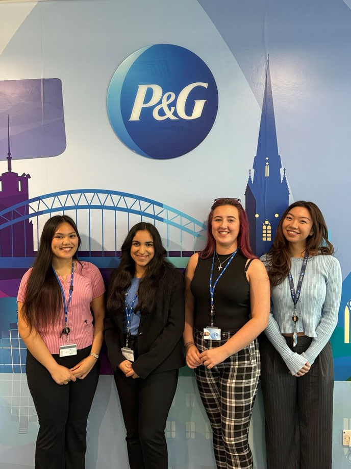 Four students in front of University logo
