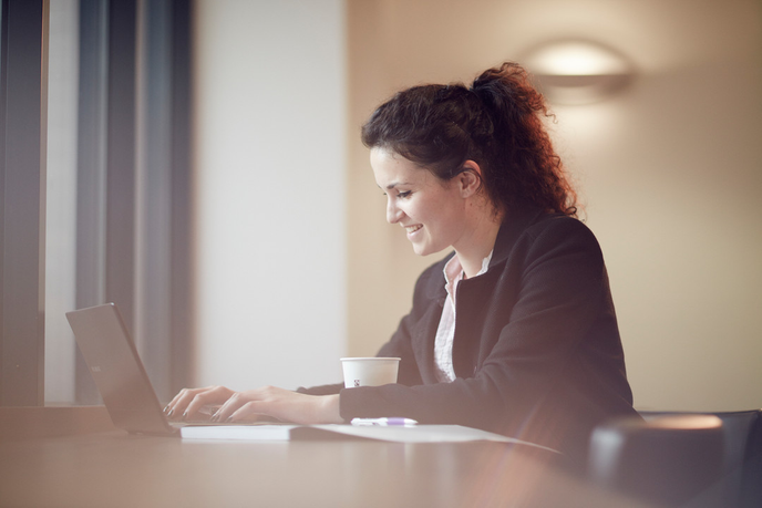 A woman in a business suit focused on her laptop, diligently working on her tasks.