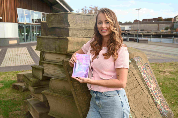 Natalie Overton holding her new book next to a statue of a pile of books at the University of Sunderland’s St Peter’s Campus