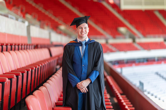 Sports Journalism graduate Rob Rush in the stands at the Stadium of Light wearing a graduation cap and gown