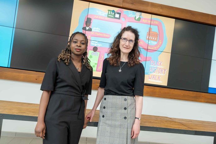 Professor Angela Smith and graduate Endurance Idowu standing infront of a colourful map of the Black History Walk