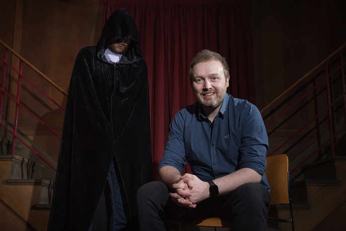 Academic sat in front of cloaked figure
