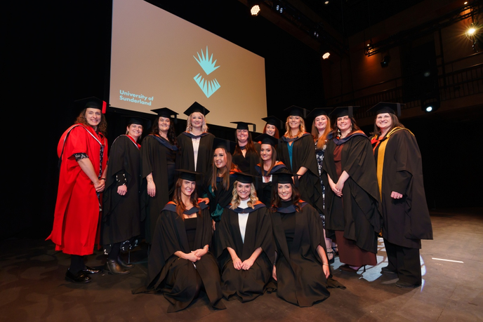 Group of graduates and academics in gowns on a stage