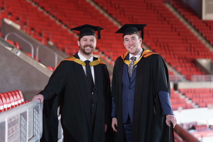 Two graduates standing in football stadium