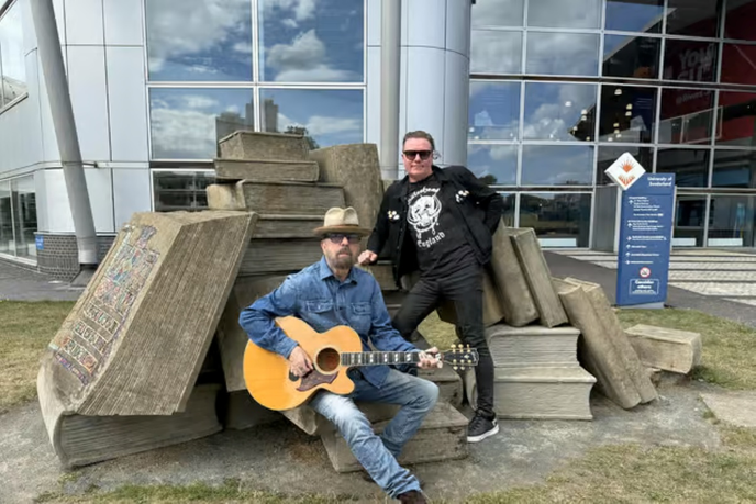 Musicians holding a guitar sat on book sculptures
