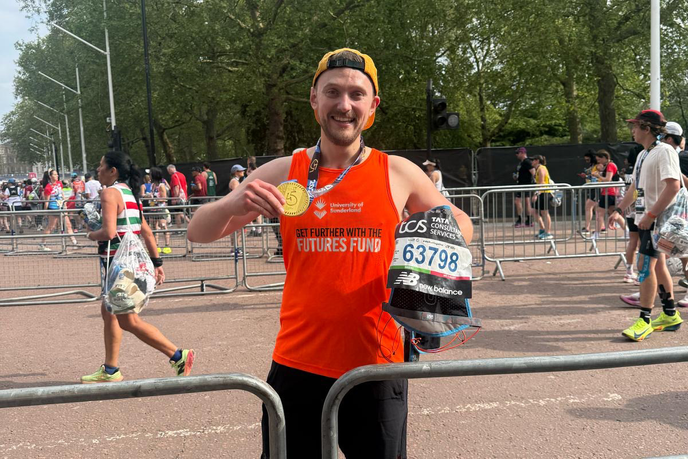 Alumnus holding medal on the street at the London Marathon
