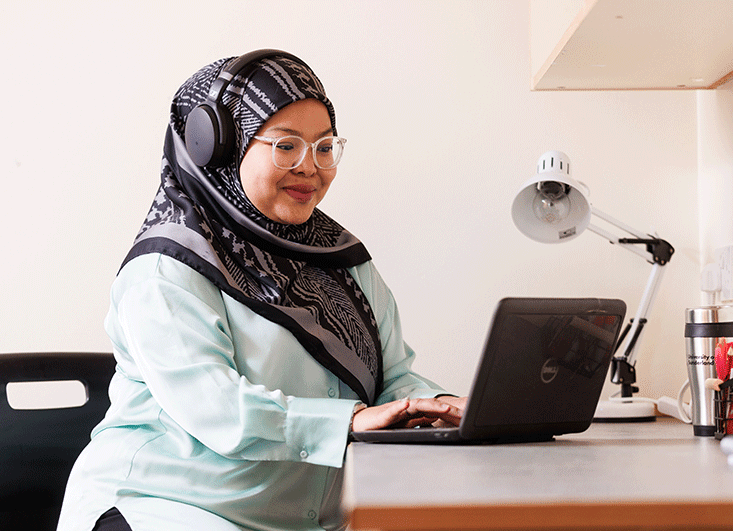 Asian female student with headscarf in her accommodation room on laptop