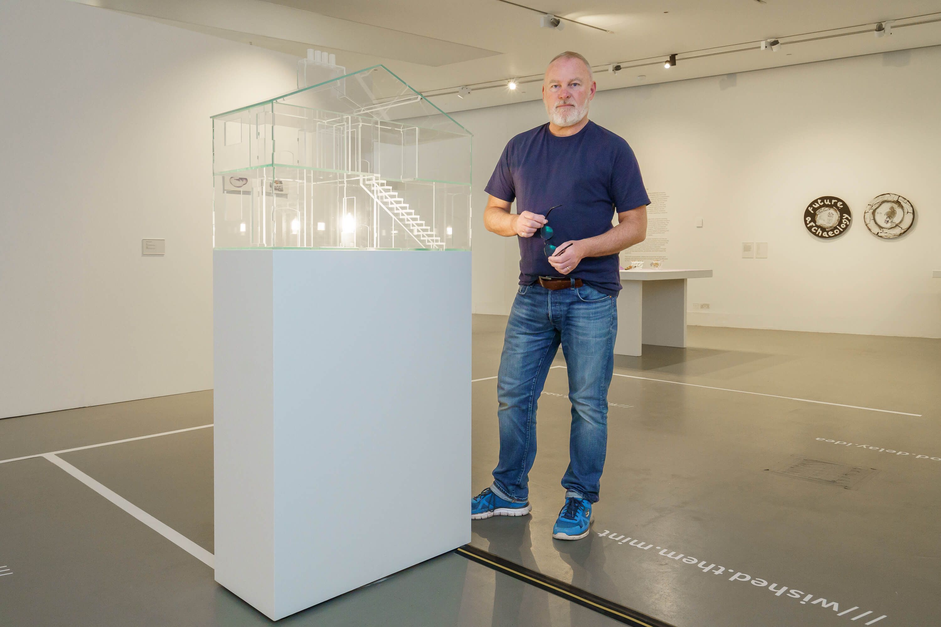 Professor Andrew Livingstone standing to the side of his exhibit in the National Glass Centre