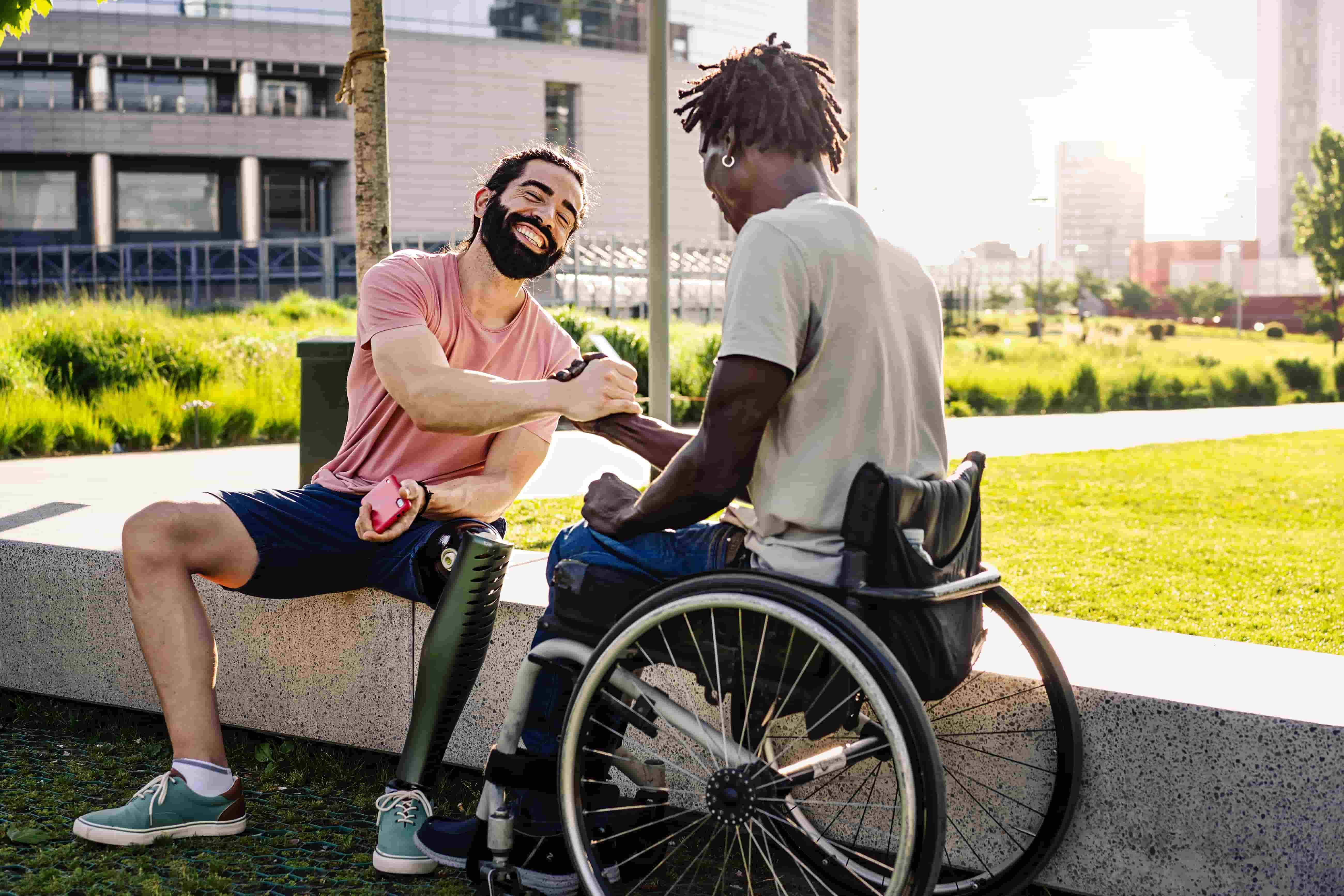 A man with a prosthetic leg shakes hands with a man in a wheelchair.