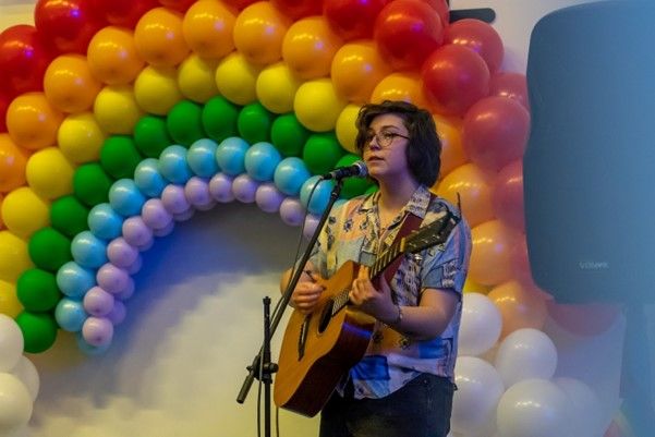 A student playing guitar in front of a rainbow balloon arch