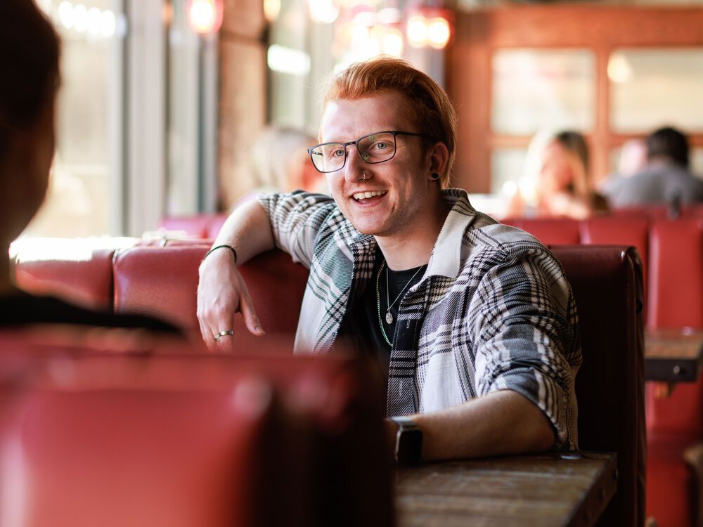 A student sitting in a booth in a restaurant smiling at someone opposite them