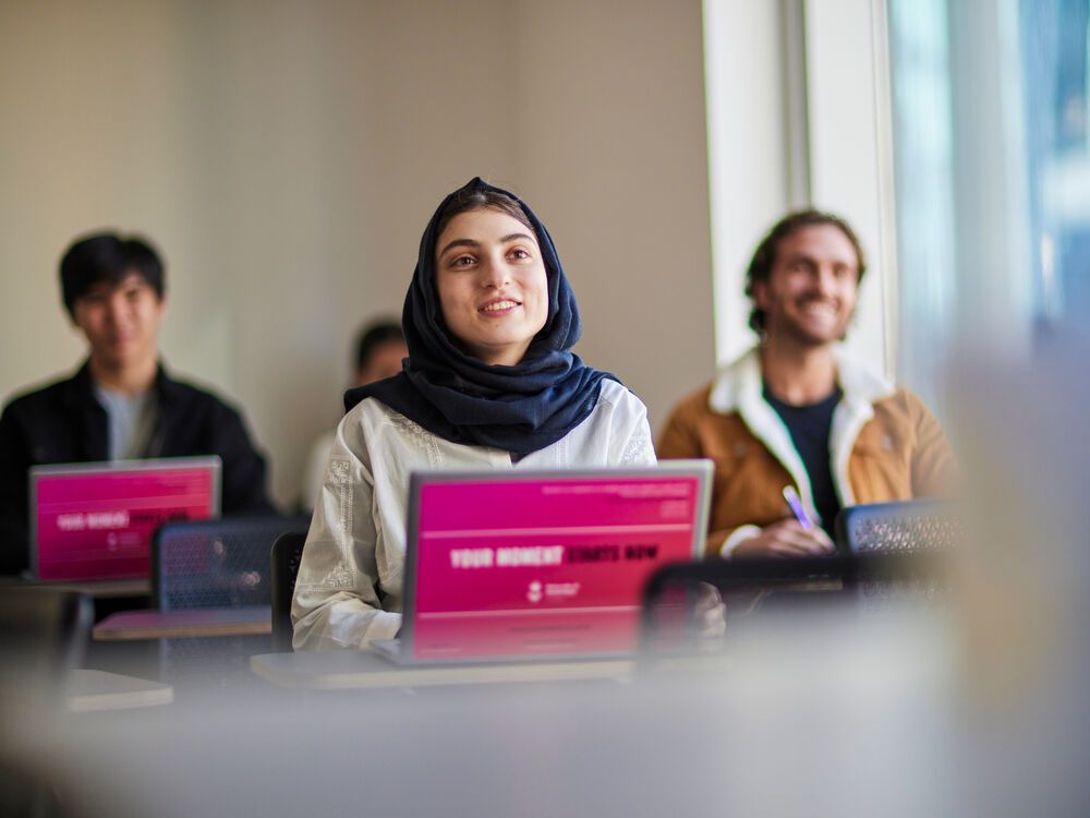 A group of students sitting in a classroom on laptops during a class