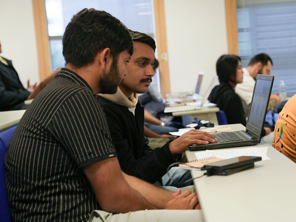 Two students working together at a laptop during a lecture