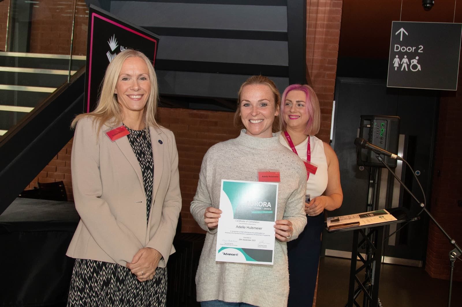 Three members of University of Sunderland staff who attended the Aurora Celebration at Firestation smiling to camera, one holding a certificate