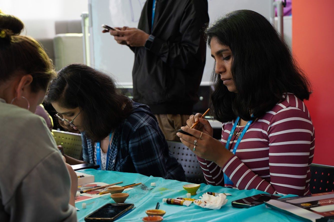 Three students sitting together at a table painting objects for Diwali