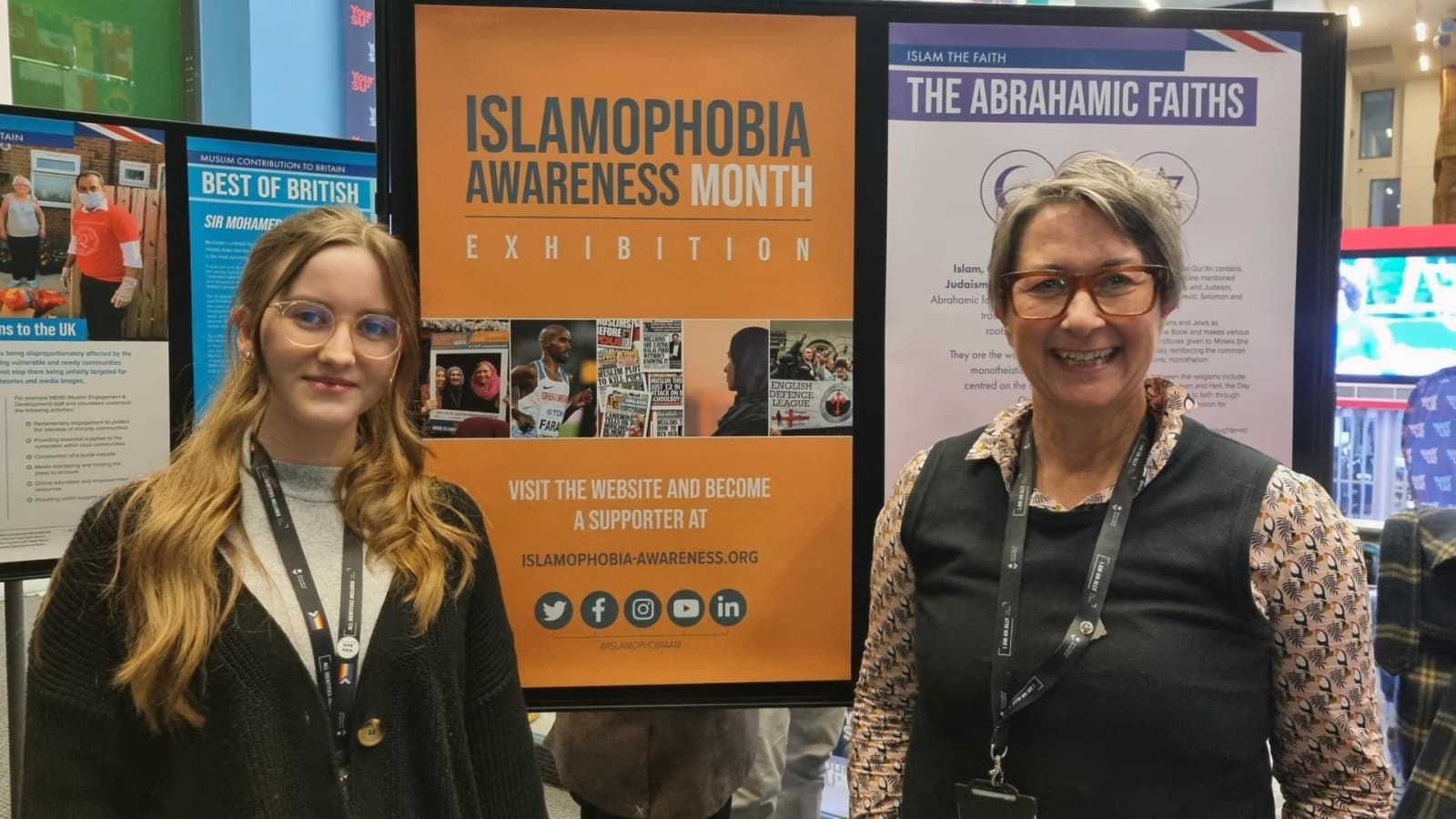 Two staff members standing in front of an Islamaphobia awareness sign