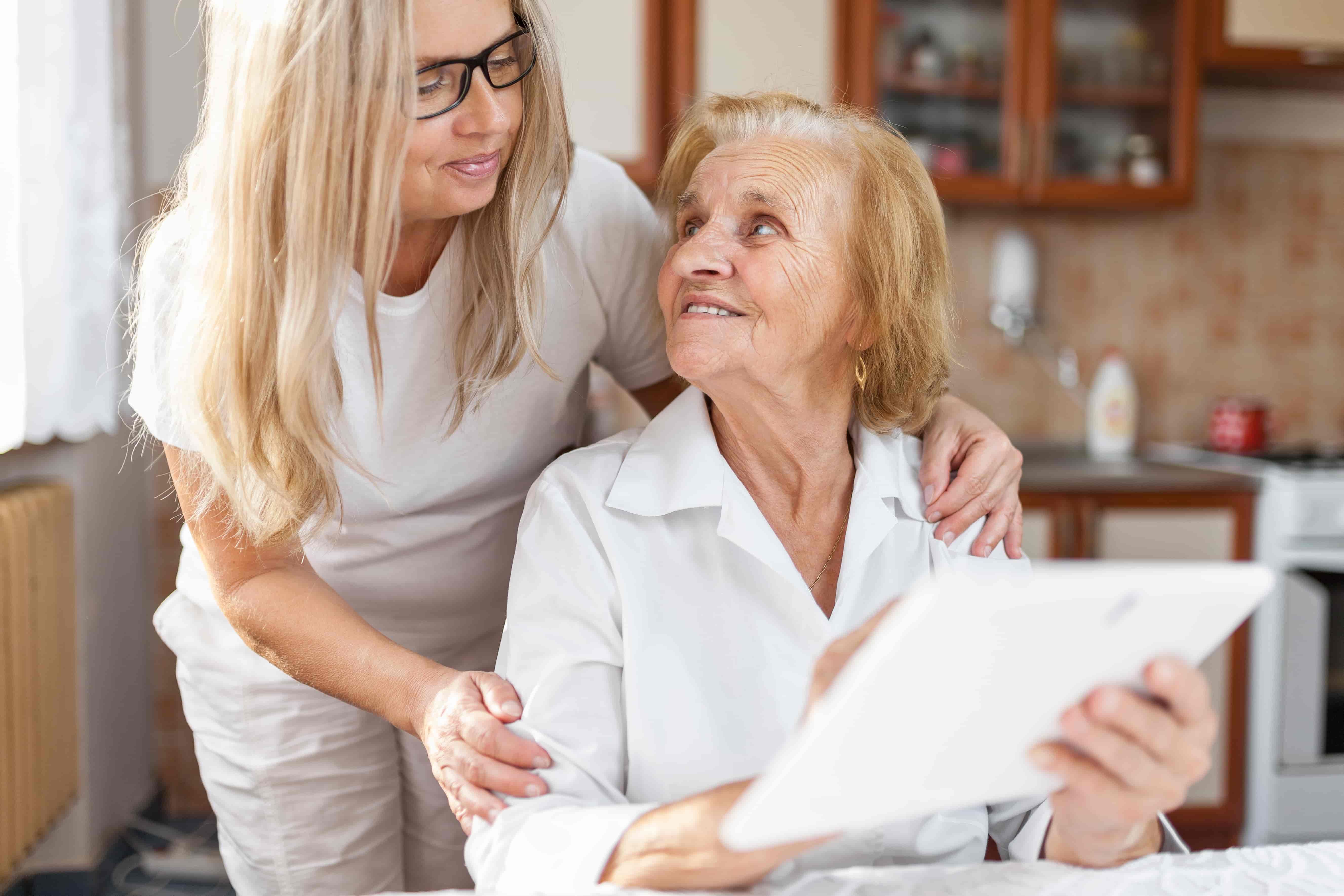 A carer leaning over the shoulder of an elderly person who is reading a document