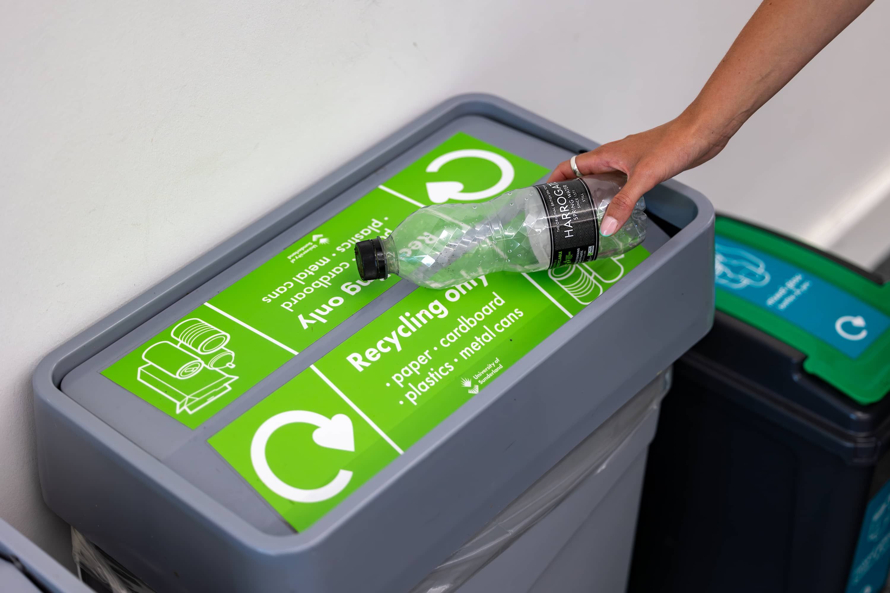 A hand leaning into the recycling bin with a empty water bottle