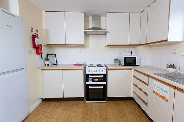 Kitchen benches with cupboards, an oven with a hob and hood next to a large fridge