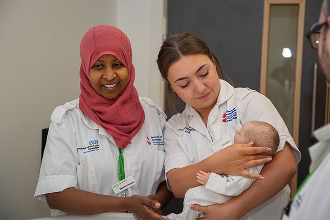 Three midwives looking at a baby that is being held by one of the midwives, smiling