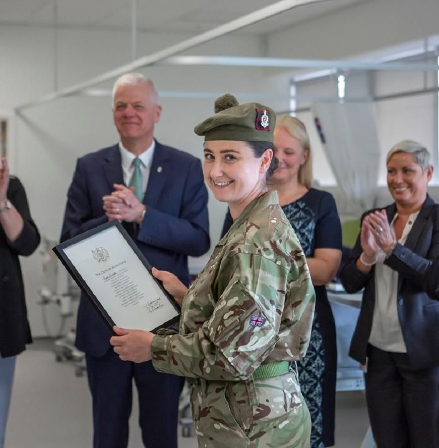 A woman in an army uniform receives a certificate while people applaud