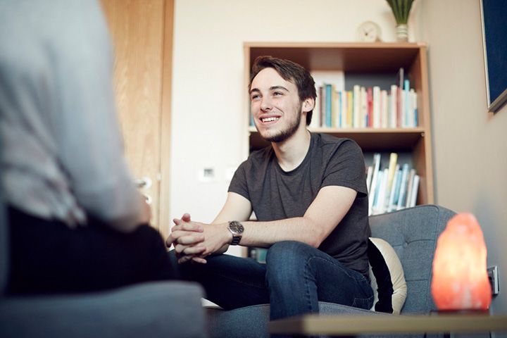 A young man sitting in a chair smiling and talking to another person off camera