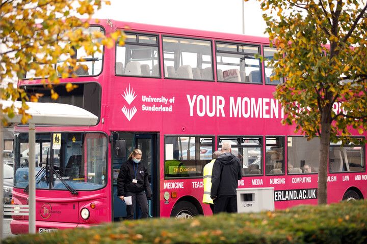 A pink double decker bus parked outside of the bus stop at City Campus