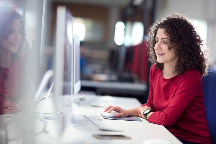 A student sitting at a desktop computer with her hand on the mouse