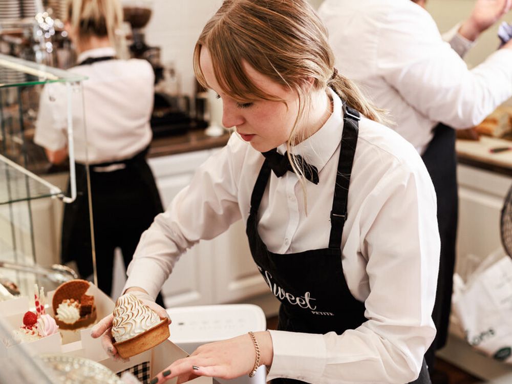 A young person working behind a cafe counter, putting a cake in a box