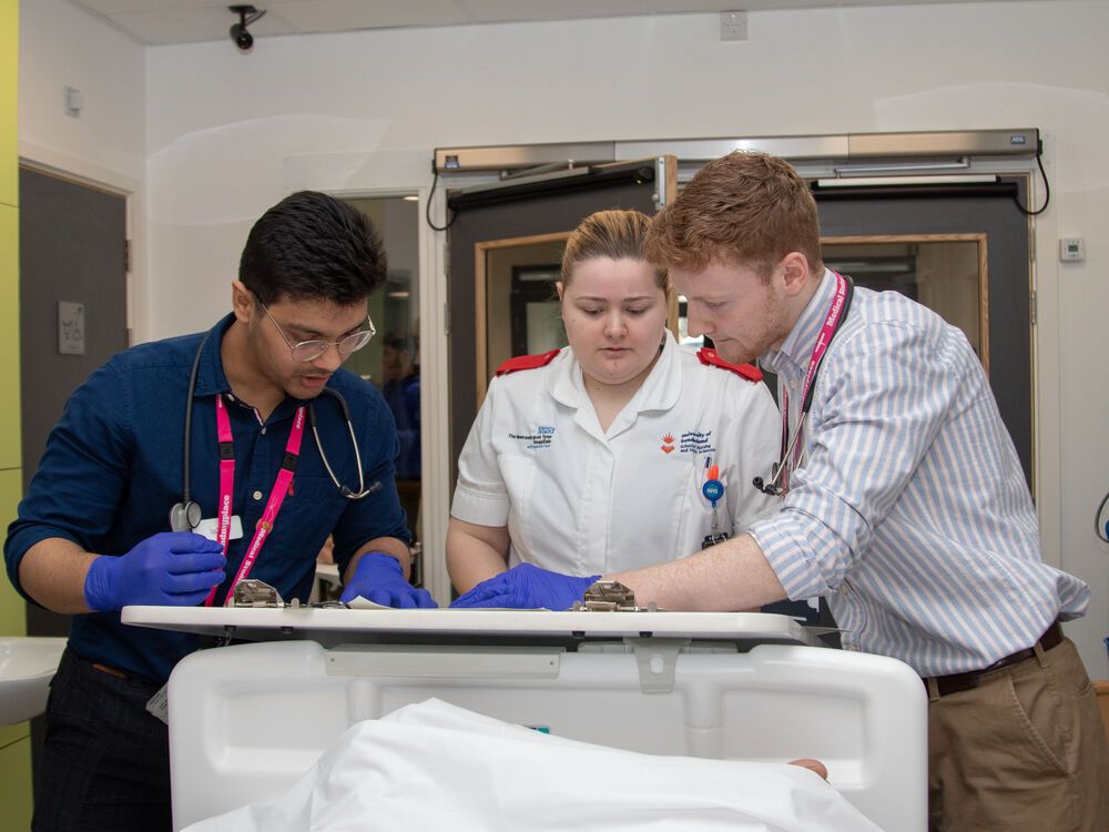 A nursing student and two medicine students examining a patient together in a mock ward