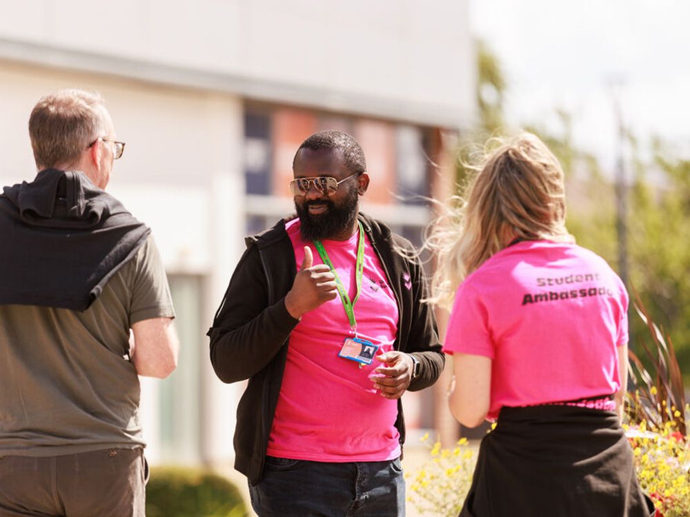 Two Student Ambassadors talking to a parent outside on campus