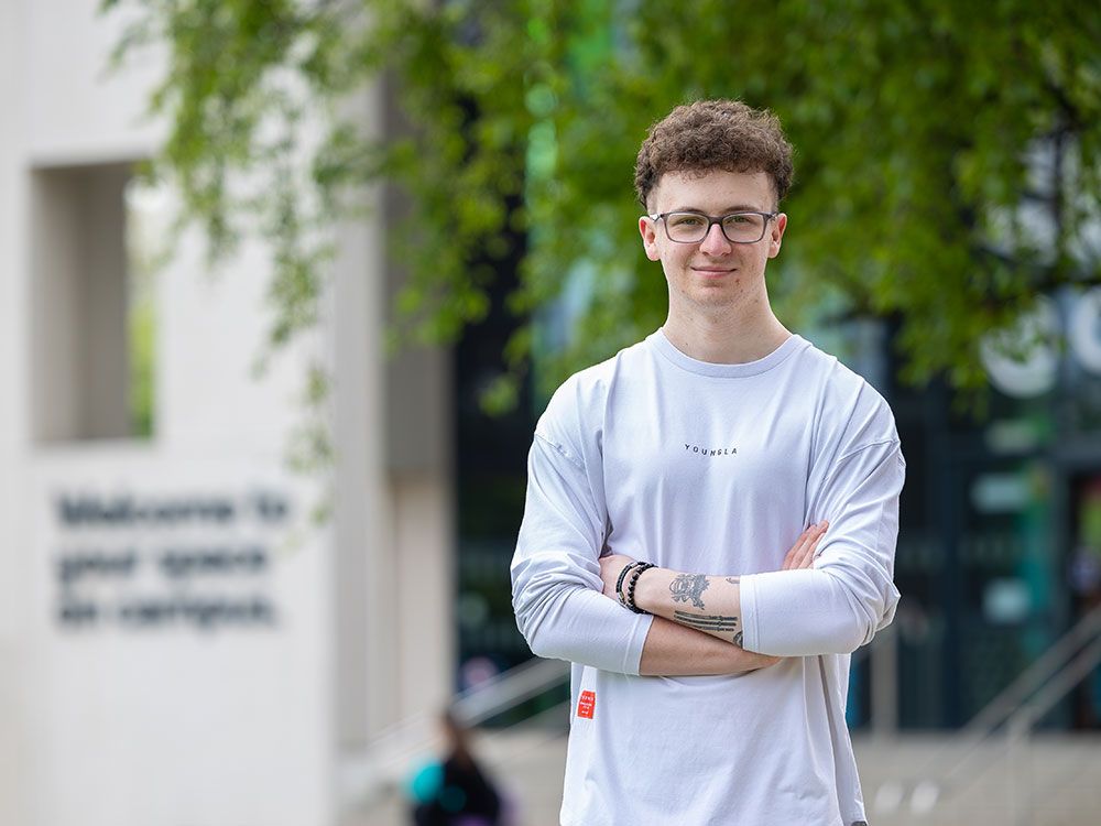 A student standing in front of CitySpace, smiling to camera with their arms folded in a confident way