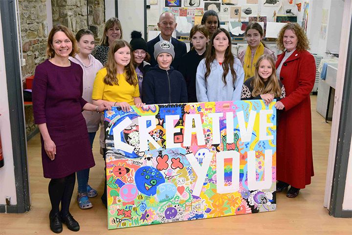 School pupils and University art staff standing around a colourful poster saying 'Creative You'